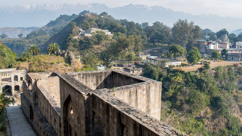 A historical stone bridge with arches, a lush green hillside, and a distant mountain range.