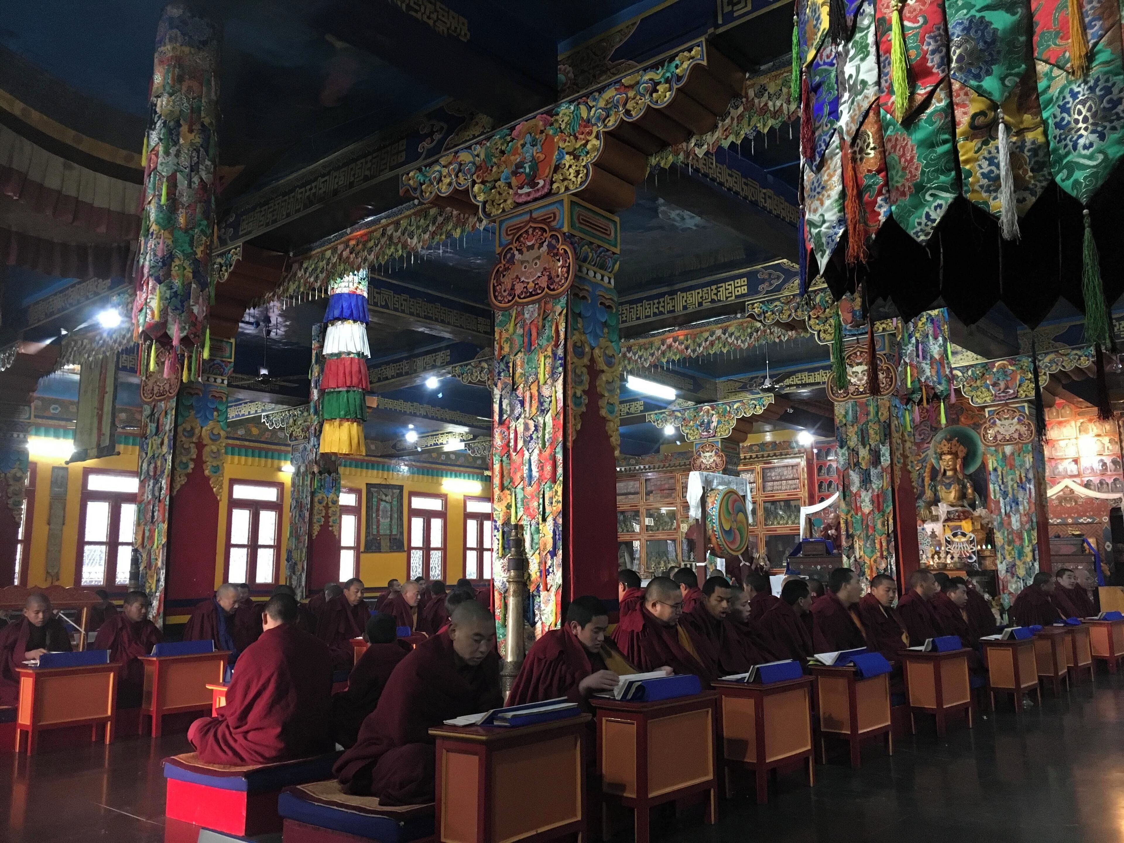 A brightly decorated hall with monks studying.