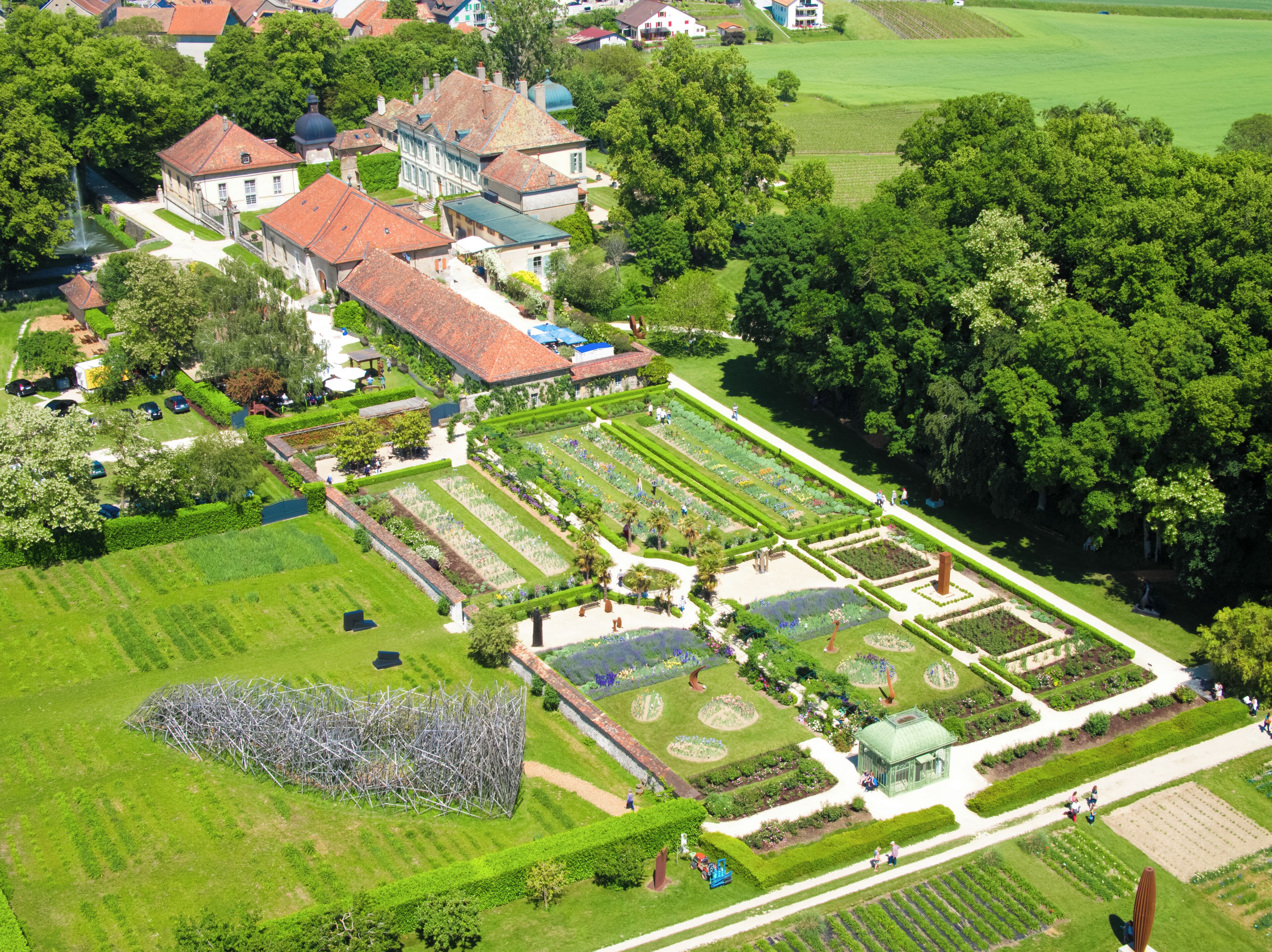 An aerial view of a well-maintained garden with geometrically arranged flower beds and a variety of trees.