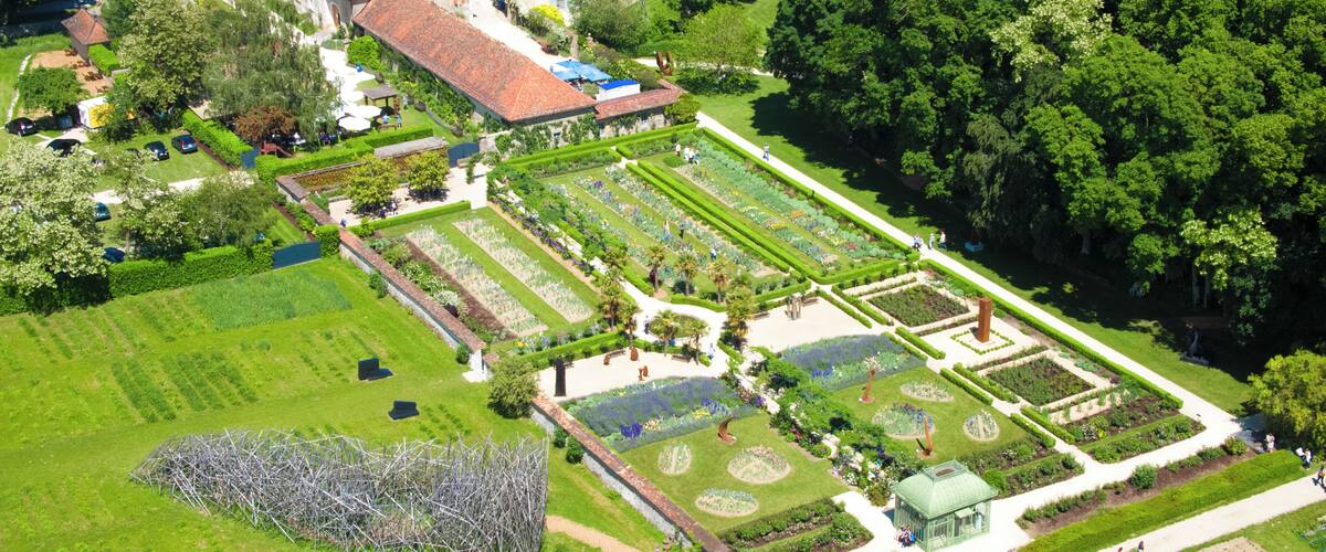 An aerial view of a well-maintained garden with geometrically arranged flower beds and a variety of trees.