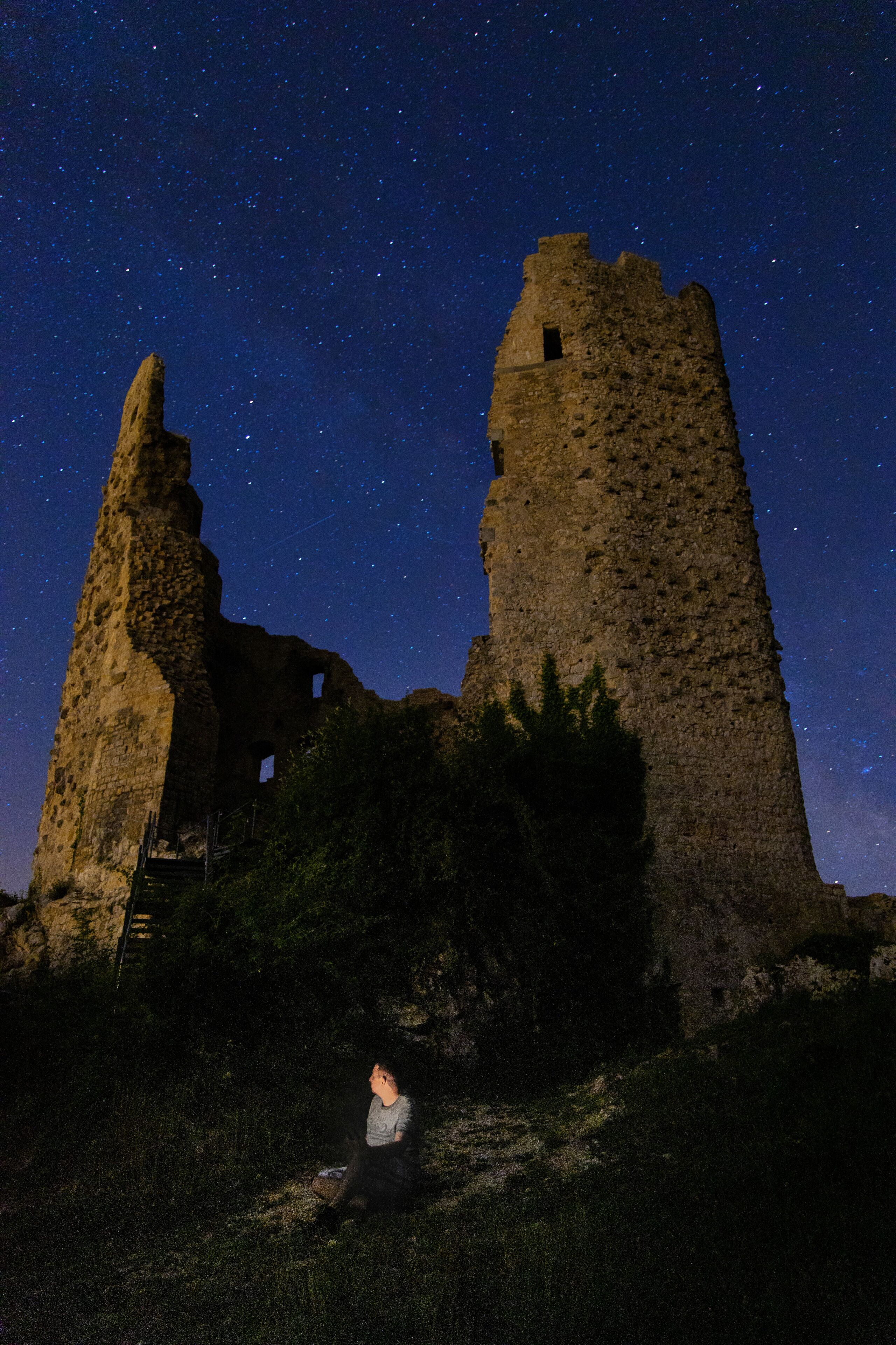 A starry night sky over ancient ruins with a person sitting in the foreground.