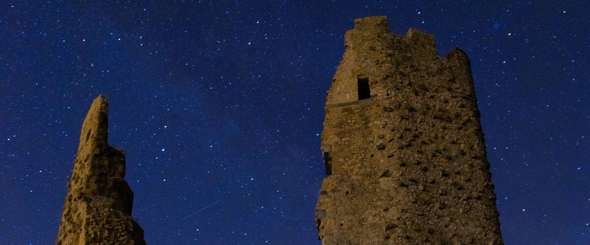 A starry night sky over ancient ruins with a person sitting in the foreground.
