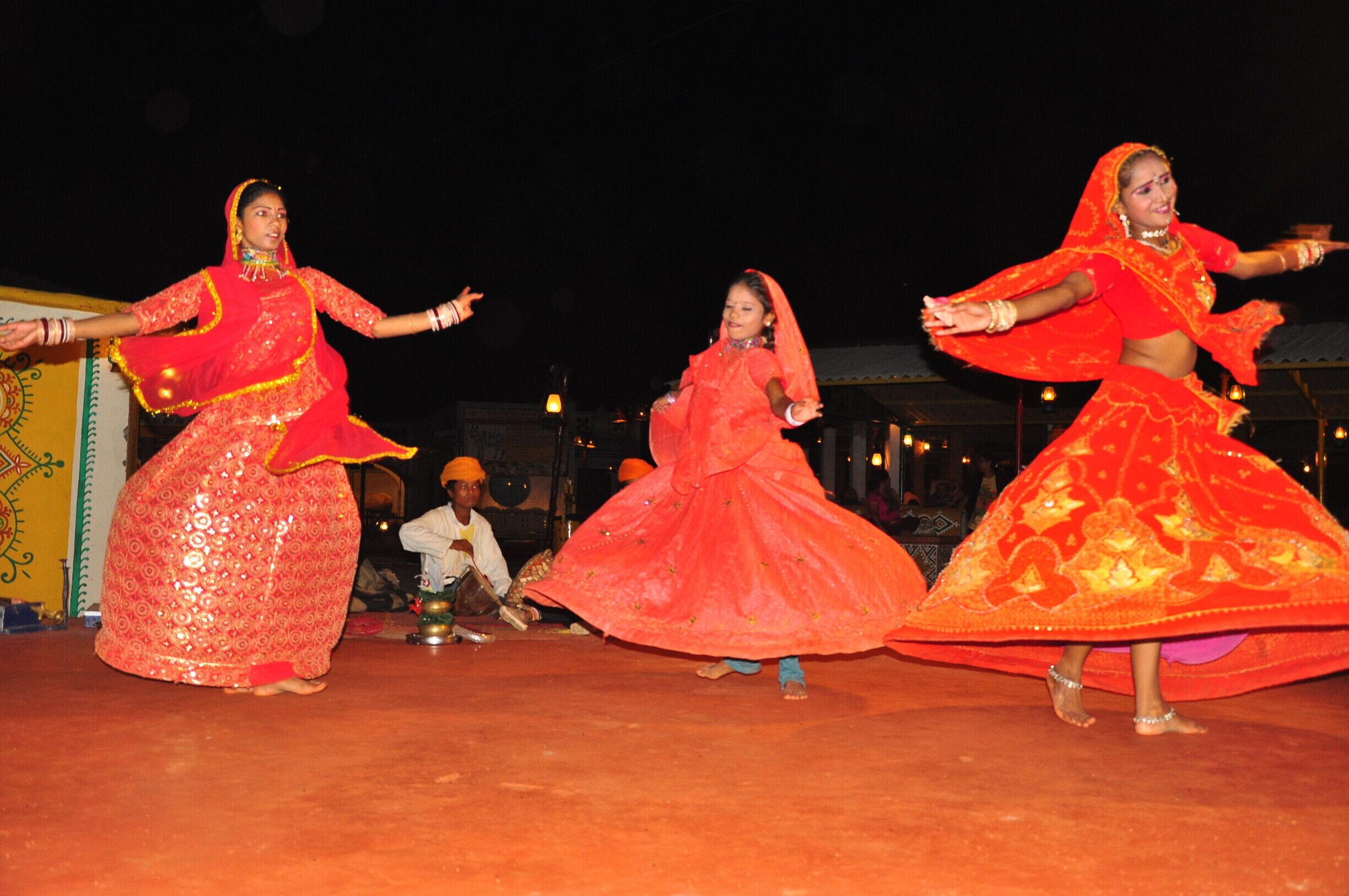 Three women in traditional red attire performing a dance on a stage.