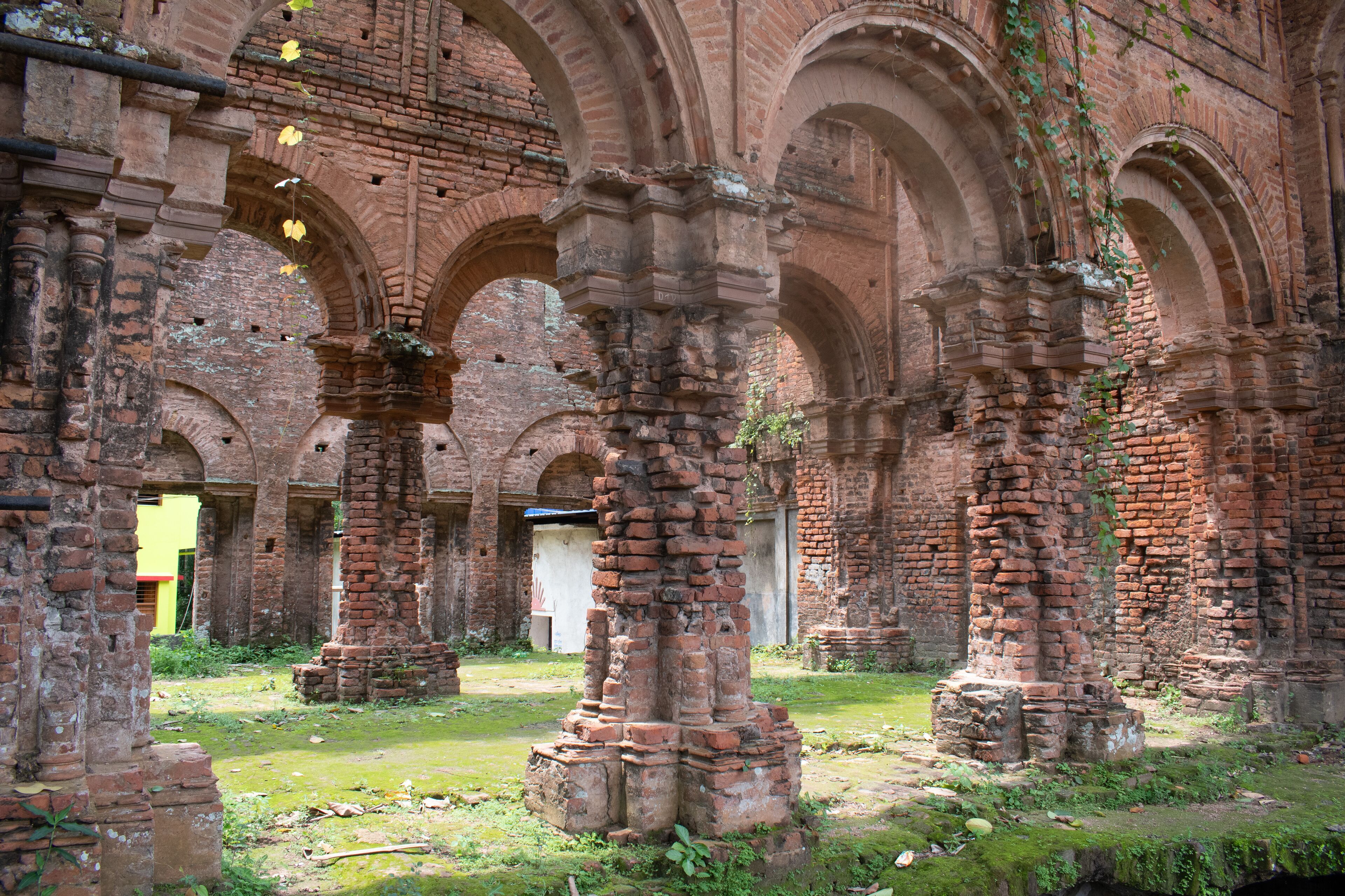 Ancient brick ruins with arches and columns, overgrown with vegetation.