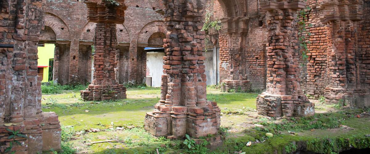 Ancient brick ruins with arches and columns, overgrown with vegetation.