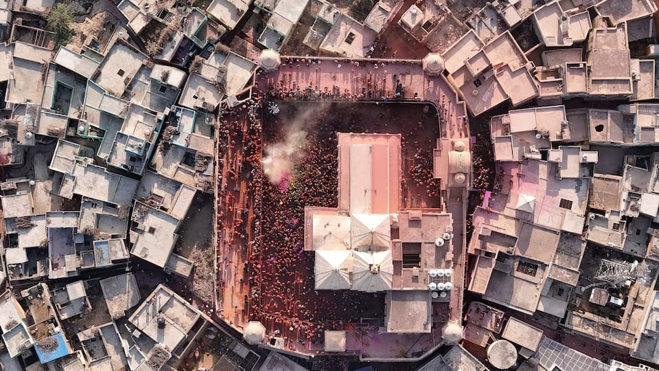 An aerial view of a densely packed urban area with numerous buildings, a central open space with a large structure, and a crowd of people.