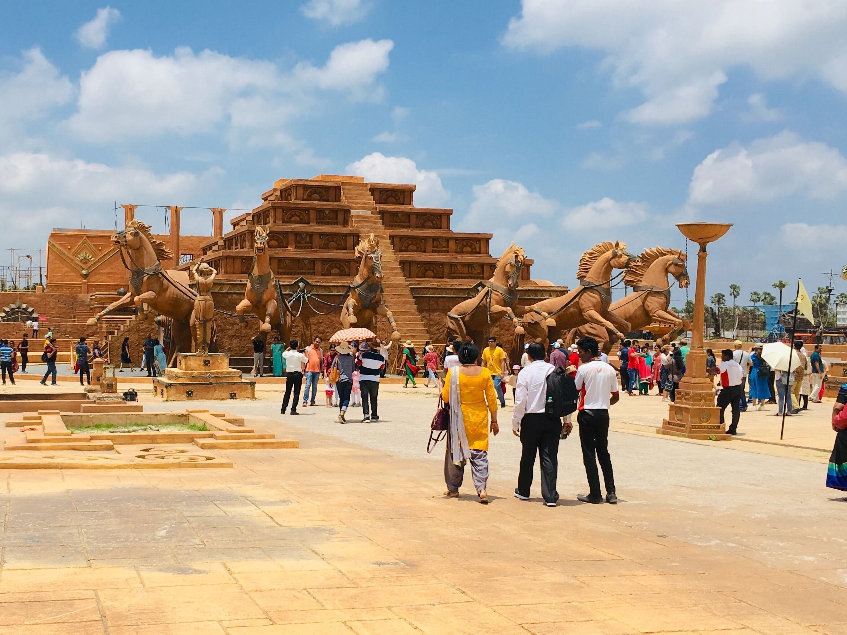 A large outdoor sculpture of horses and a pyramid-like structure with tourists.