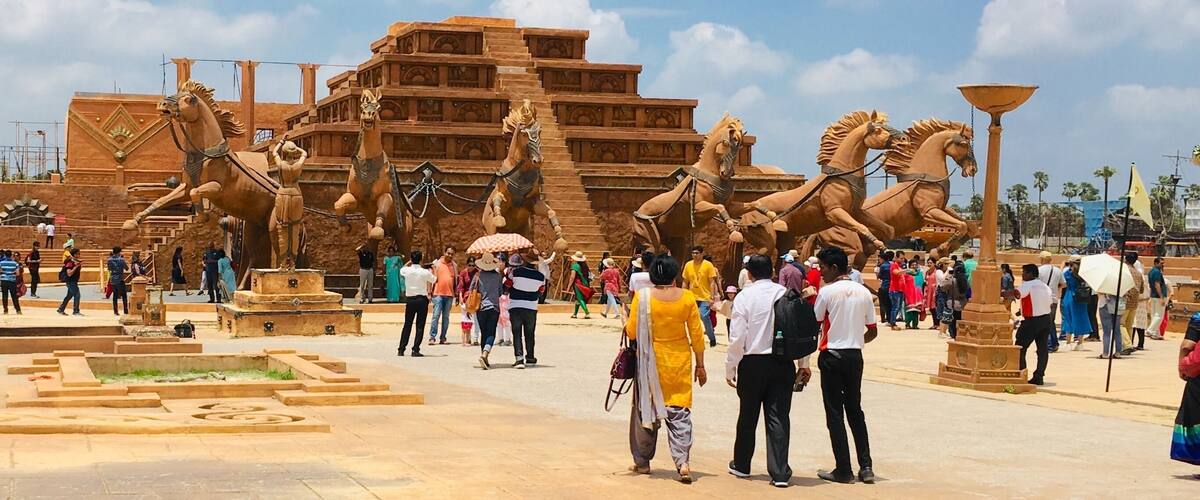 A large outdoor sculpture of horses and a pyramid-like structure with tourists.