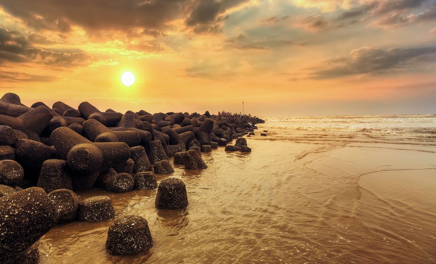 A rocky shoreline with the sun setting behind a line of rocks.