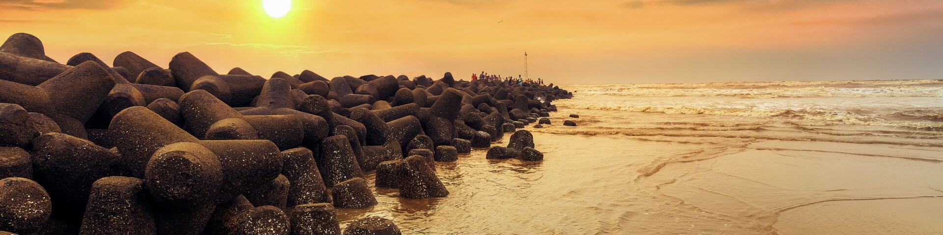 Una costa rocosa con el sol poniéndose tras una hilera de rocas.