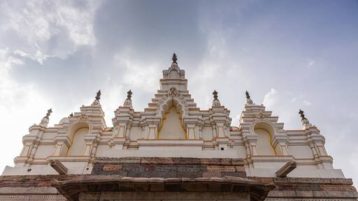 Bagalkot, Karnataka, India - November 8, 2013: Sri Sangameshwar Temple. Sculpted top in white with yellow trim on top of brown stone building under gray cloudscape.