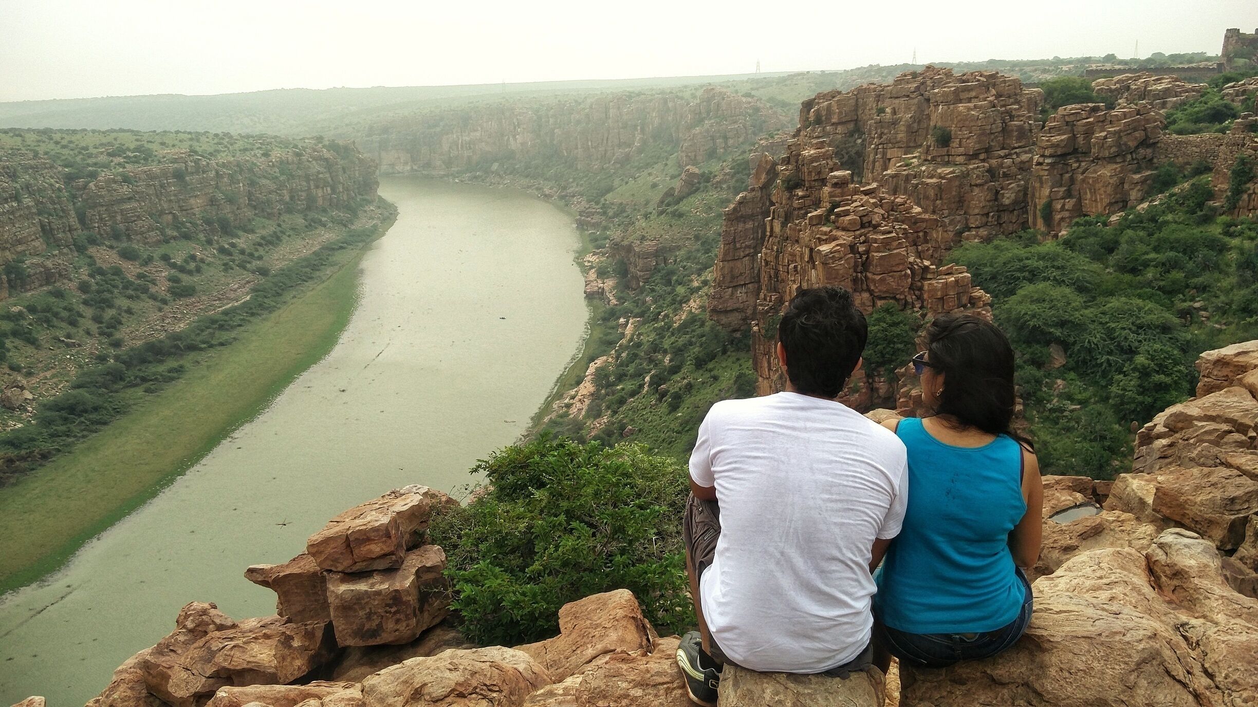 A couple sitting on a rocky outcrop overlooking a river canyon.