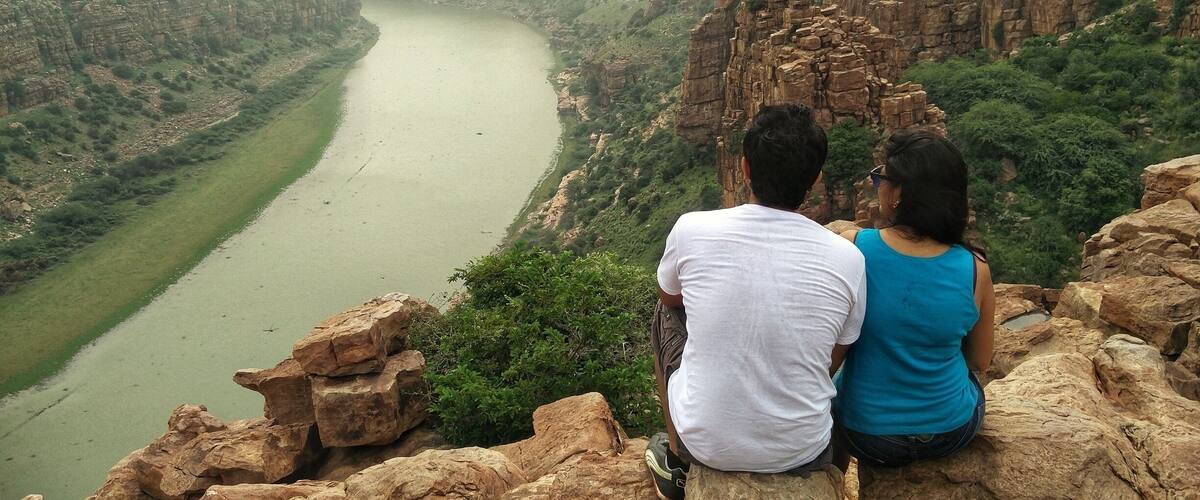 A couple sitting on a rocky outcrop overlooking a river canyon.