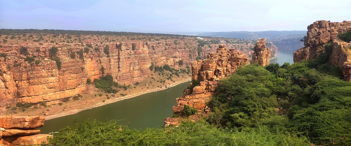 A canyon with a river, rocky cliffs, and sparse vegetation.