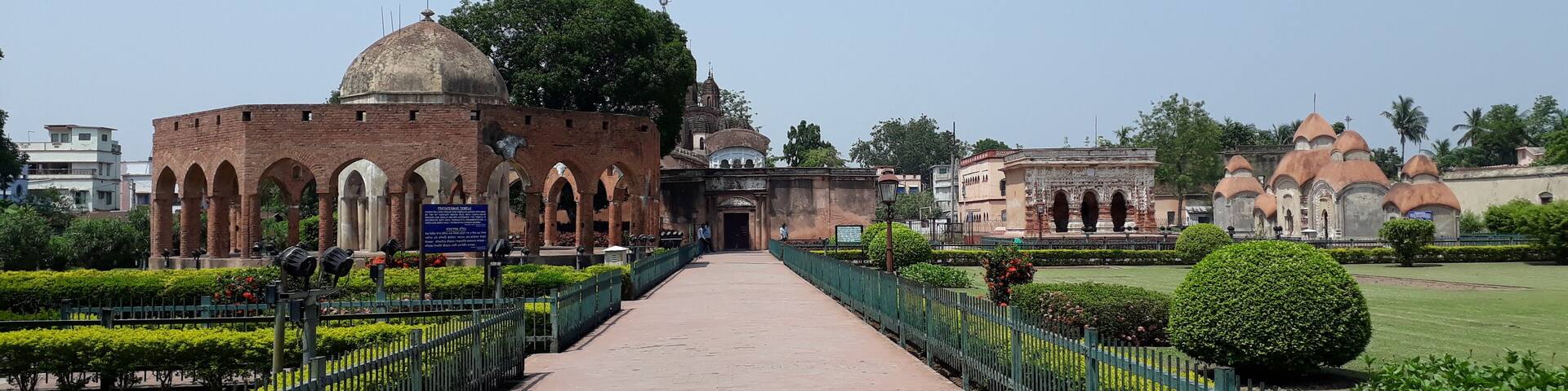 A pathway leading to a historic building with arches and domes, surrounded by well-maintained gardens and a clear sky.