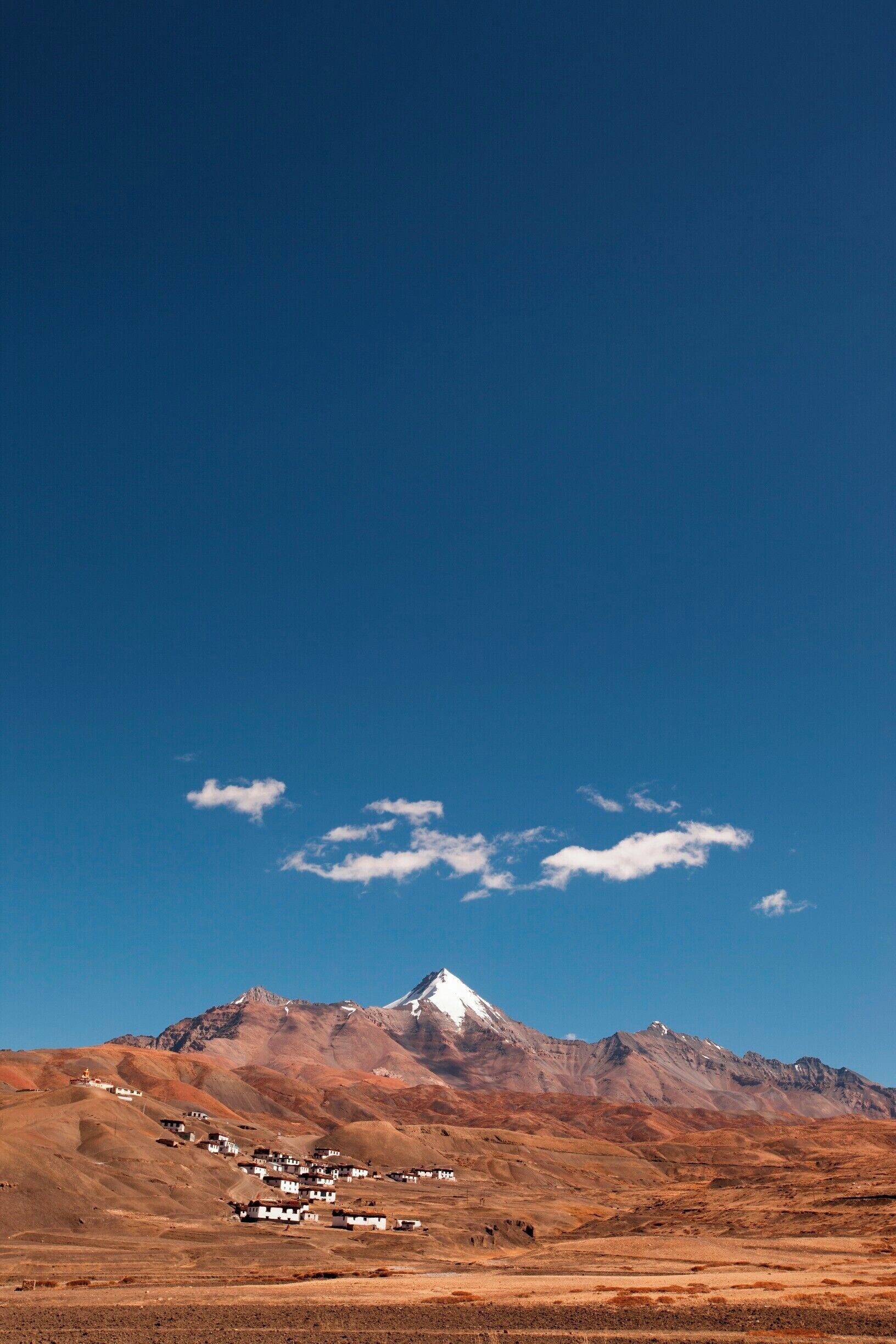 A mountain range with a snow-capped peak and a small settlement at its base.