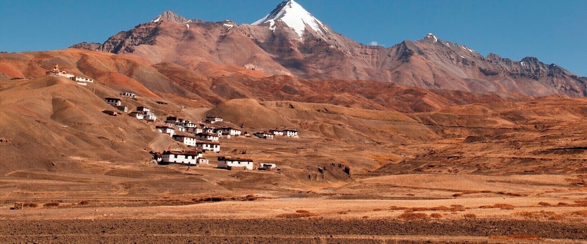 A mountain range with a snow-capped peak and a small settlement at its base.