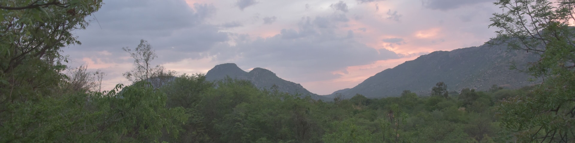 Paisagem montanhosa com vegetação verde densa e céu nublado.