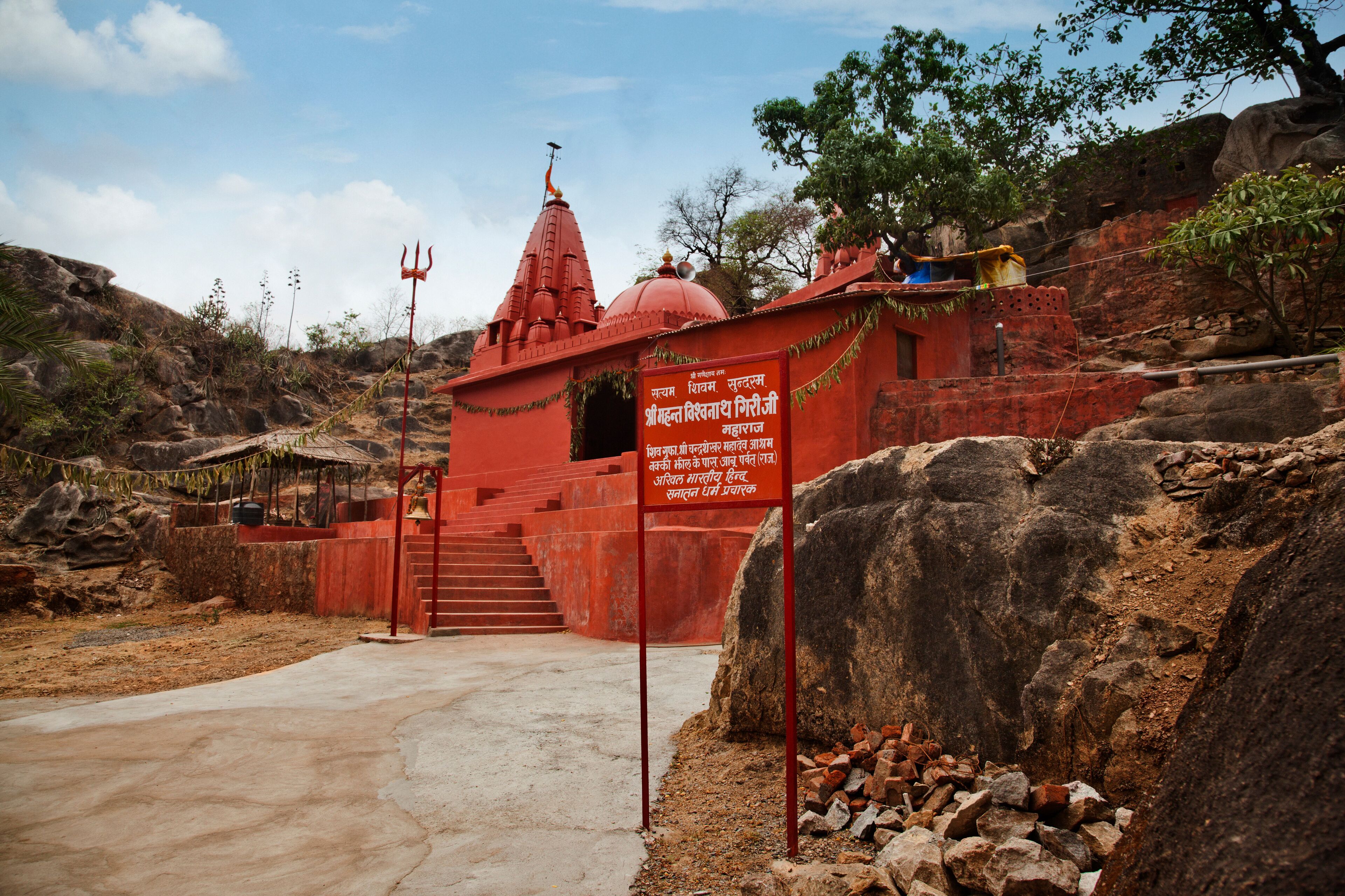 A red temple with a signboard, surrounded by rocks and trees.
