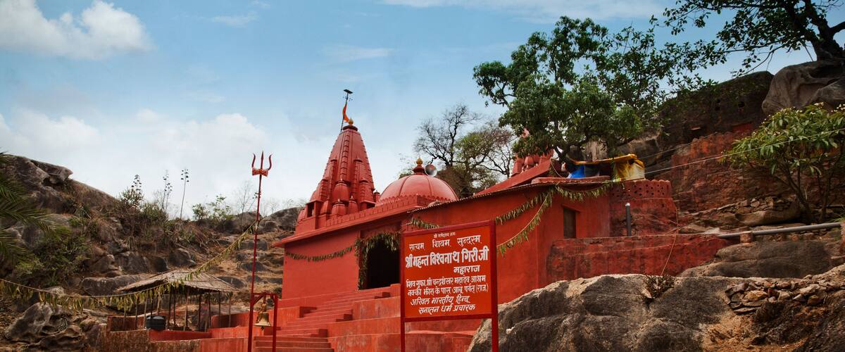 A red temple with a signboard, surrounded by rocks and trees.