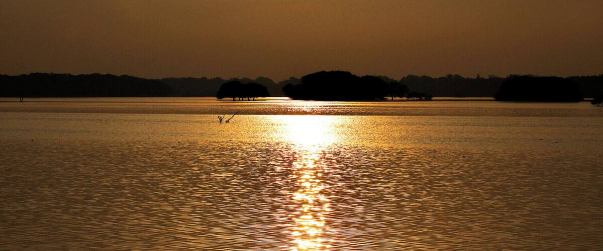 A calm lake at sunset with the sun reflecting on the water's surface.