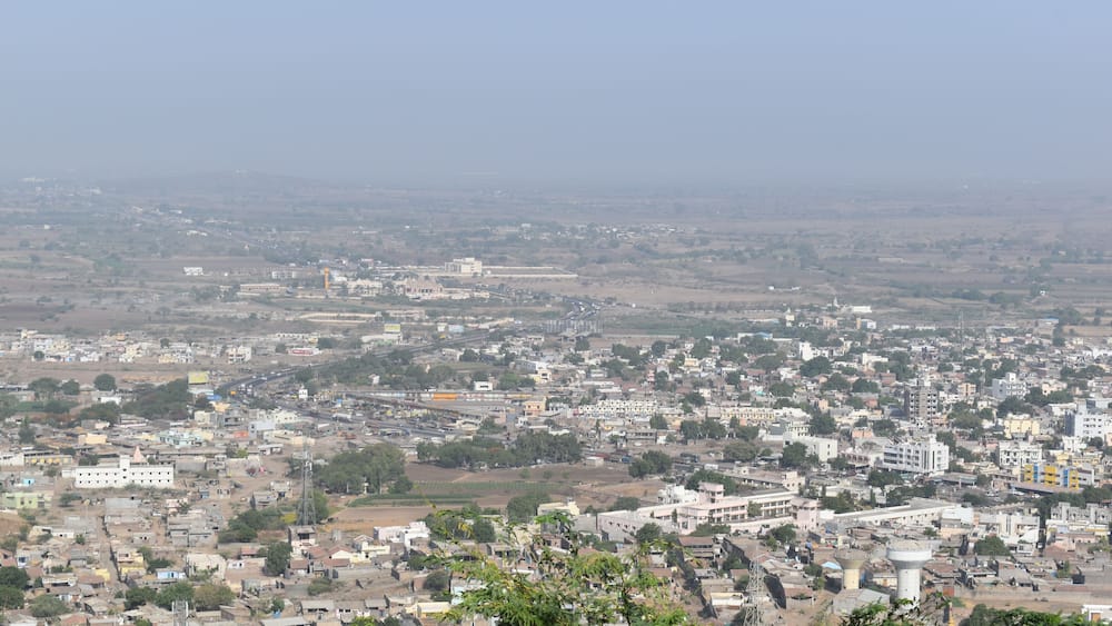 A sprawling cityscape with dense urban development, a prominent water tower, and surrounding agricultural fields.