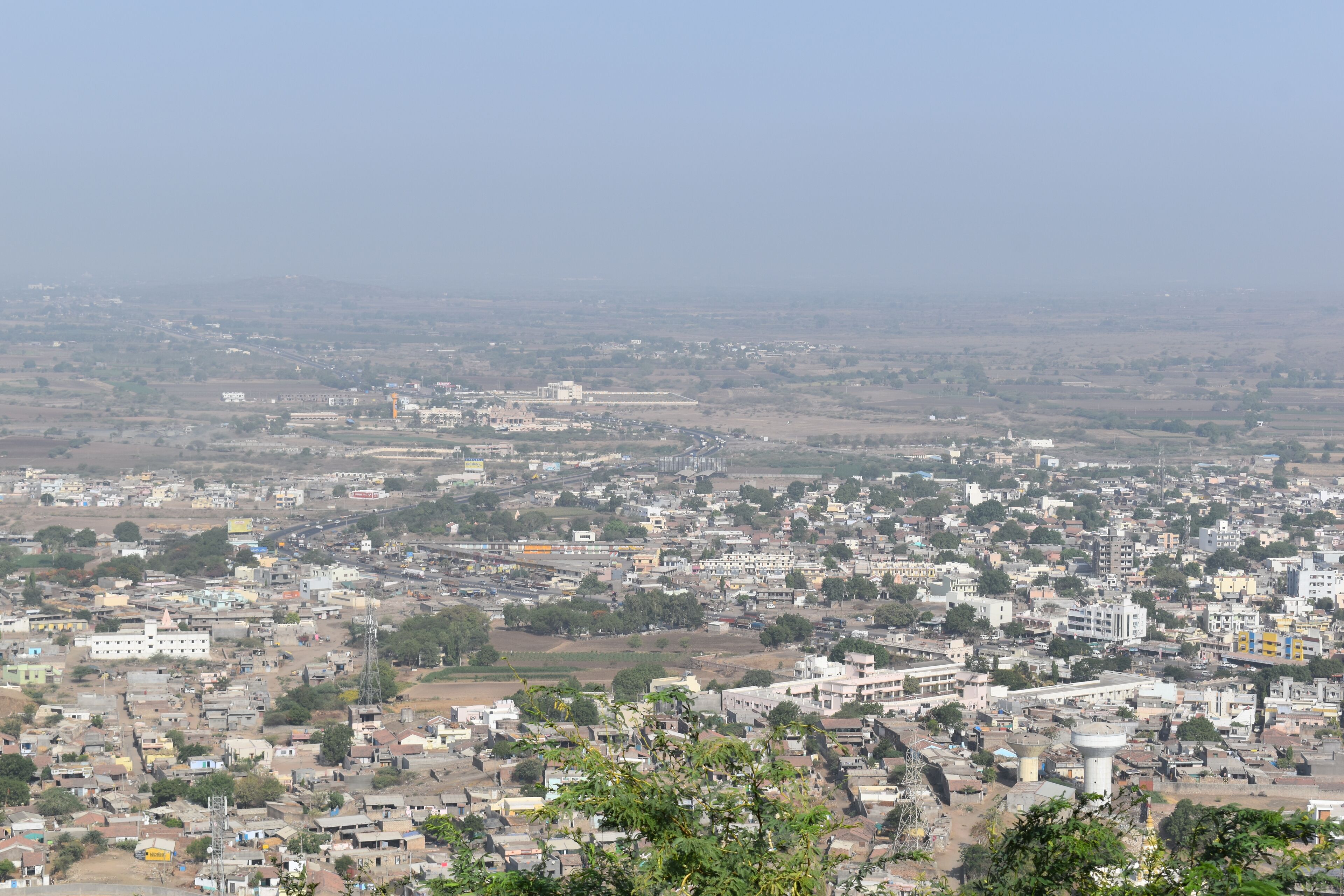 A sprawling cityscape with dense urban development, a prominent water tower, and surrounding agricultural fields.