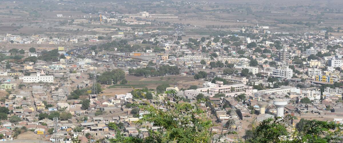 A sprawling cityscape with dense urban development, a prominent water tower, and surrounding agricultural fields.