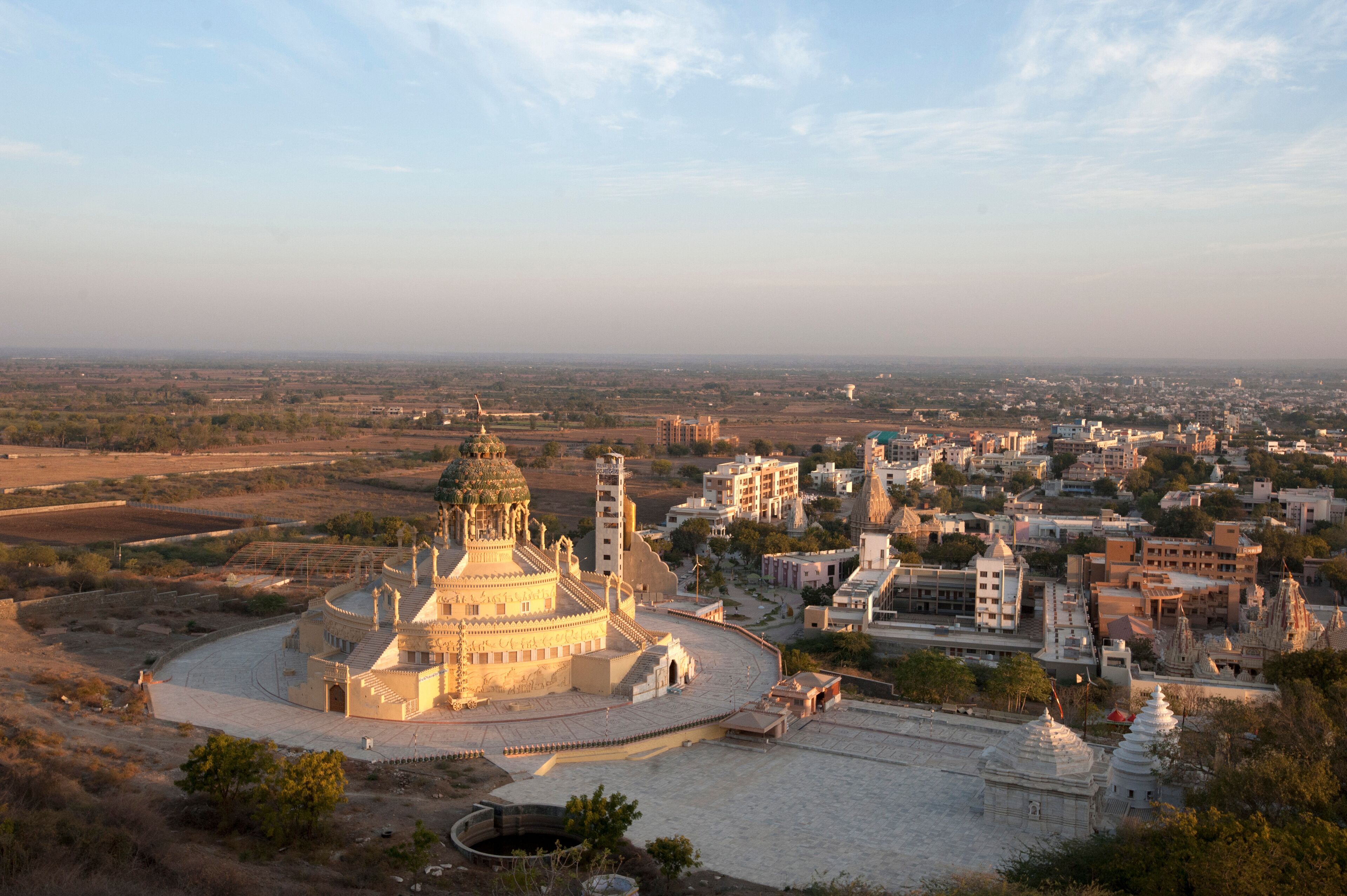 A large, ornate building with a dome and minarets, surrounded by a cityscape with various buildings and a distant view of a flat landscape.