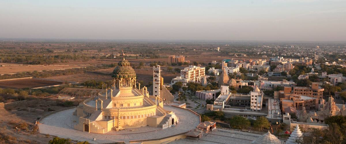 A large, ornate building with a dome and minarets, surrounded by a cityscape with various buildings and a distant view of a flat landscape.
