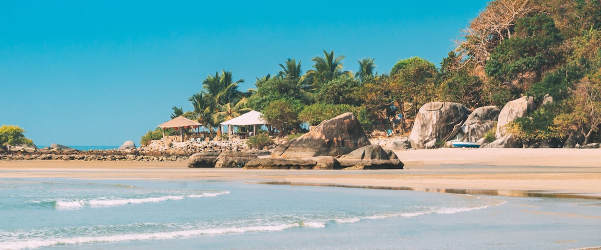 A beach with clear blue water, rocky outcrops, and palm trees.