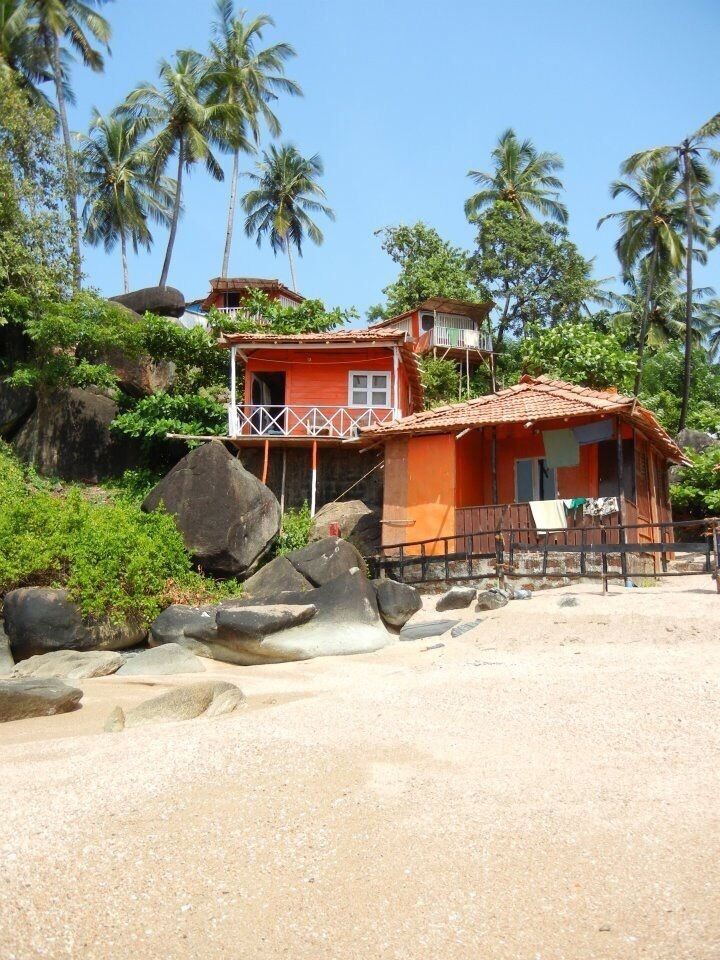 A coastal house with a red roof, surrounded by palm trees and rocks.