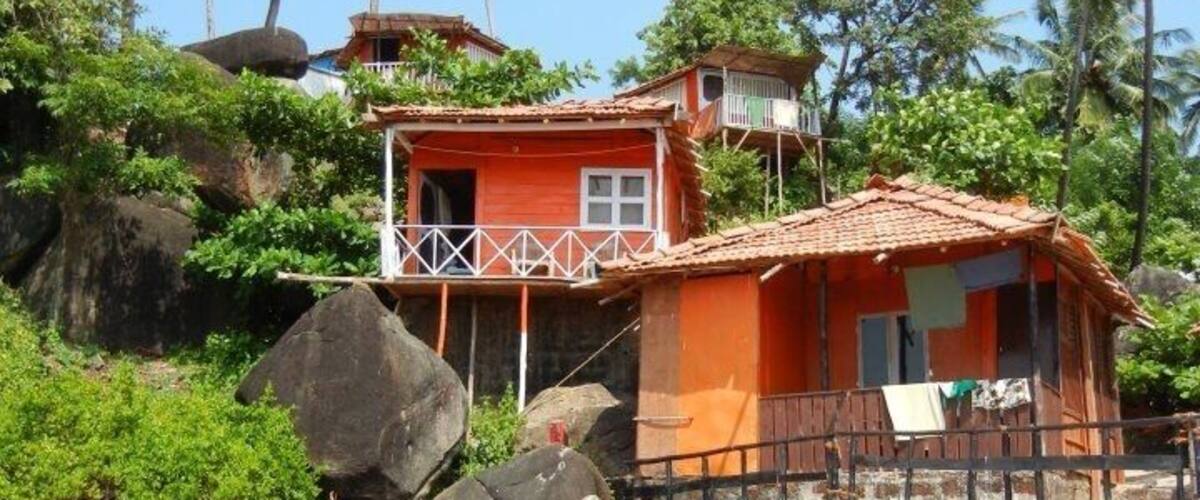A coastal house with a red roof, surrounded by palm trees and rocks.