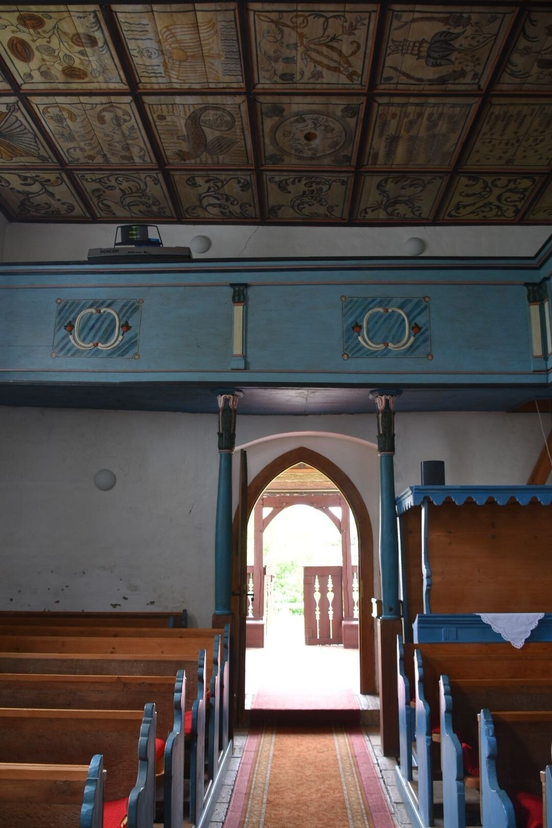 An interior with a patterned ceiling, blue walls, and a wooden bench area.