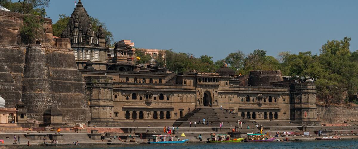 A historic temple complex with intricate architecture and a river in the foreground.