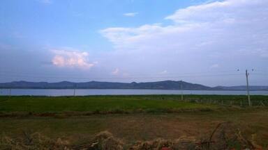 A lake with mountains in the background, surrounded by grassy fields and utility poles.