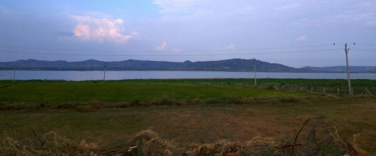 A lake with mountains in the background, surrounded by grassy fields and utility poles.