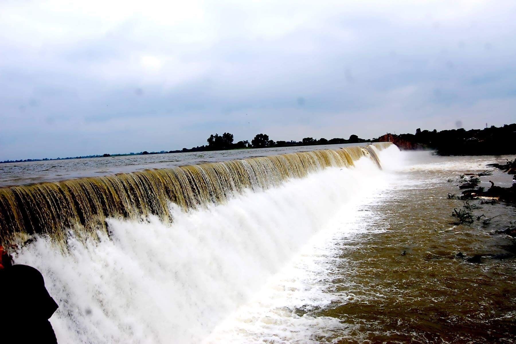 A large waterfall cascading over a concrete barrier into a river.