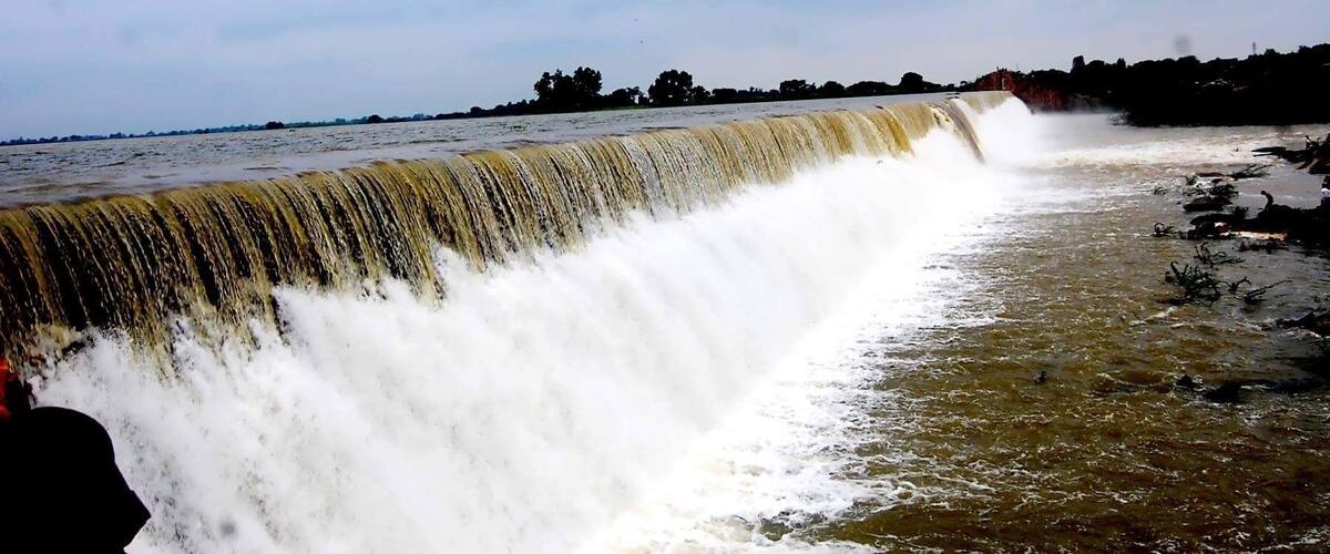 A large waterfall cascading over a concrete barrier into a river.