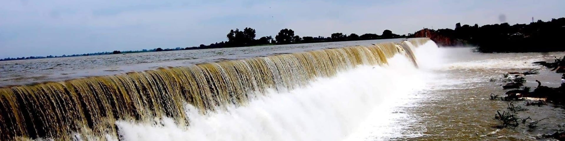 A large waterfall cascading over a concrete barrier into a river.