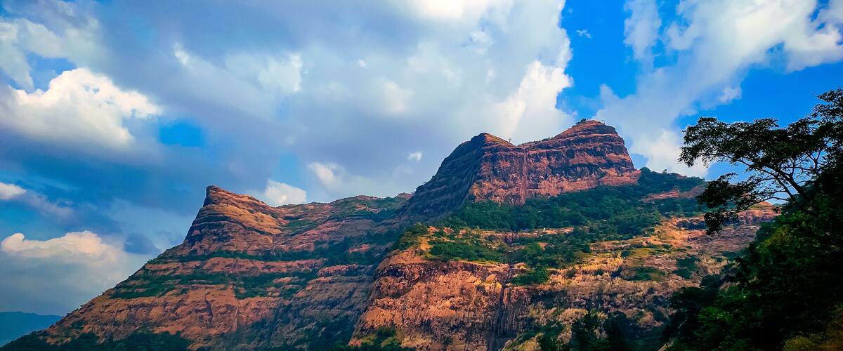 A mountain with two prominent peaks, lush green vegetation, and a partly cloudy sky.