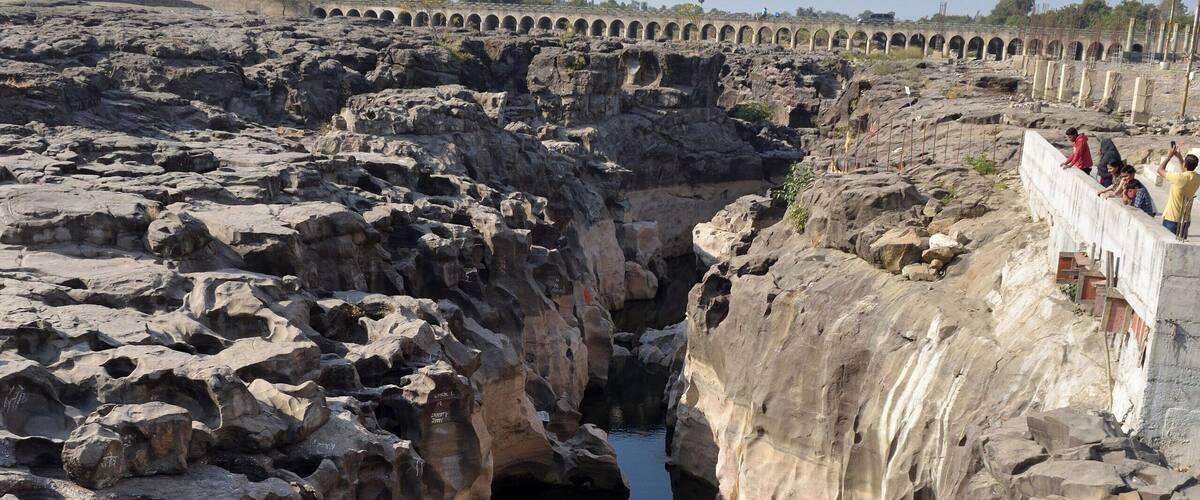 A rocky gorge with a water channel and a bridge in the background.