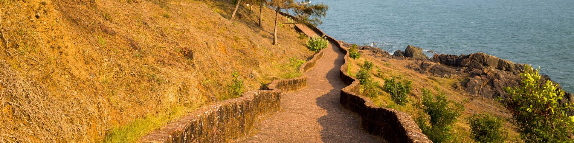 A coastal path with a brick wall on one side and a view of the ocean with boats on the water.