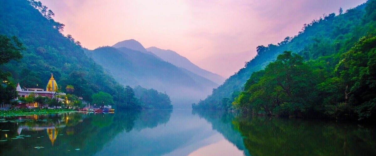 A calm river with reflections, surrounded by lush greenery and mountains in the background.