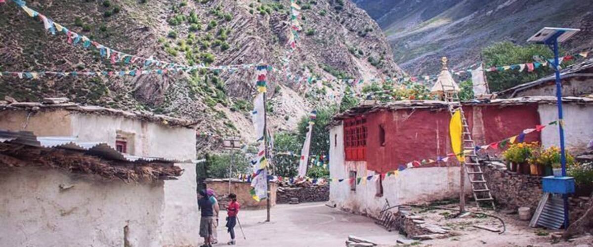 A mountainous village with traditional houses, prayer flags, and a small shrine.