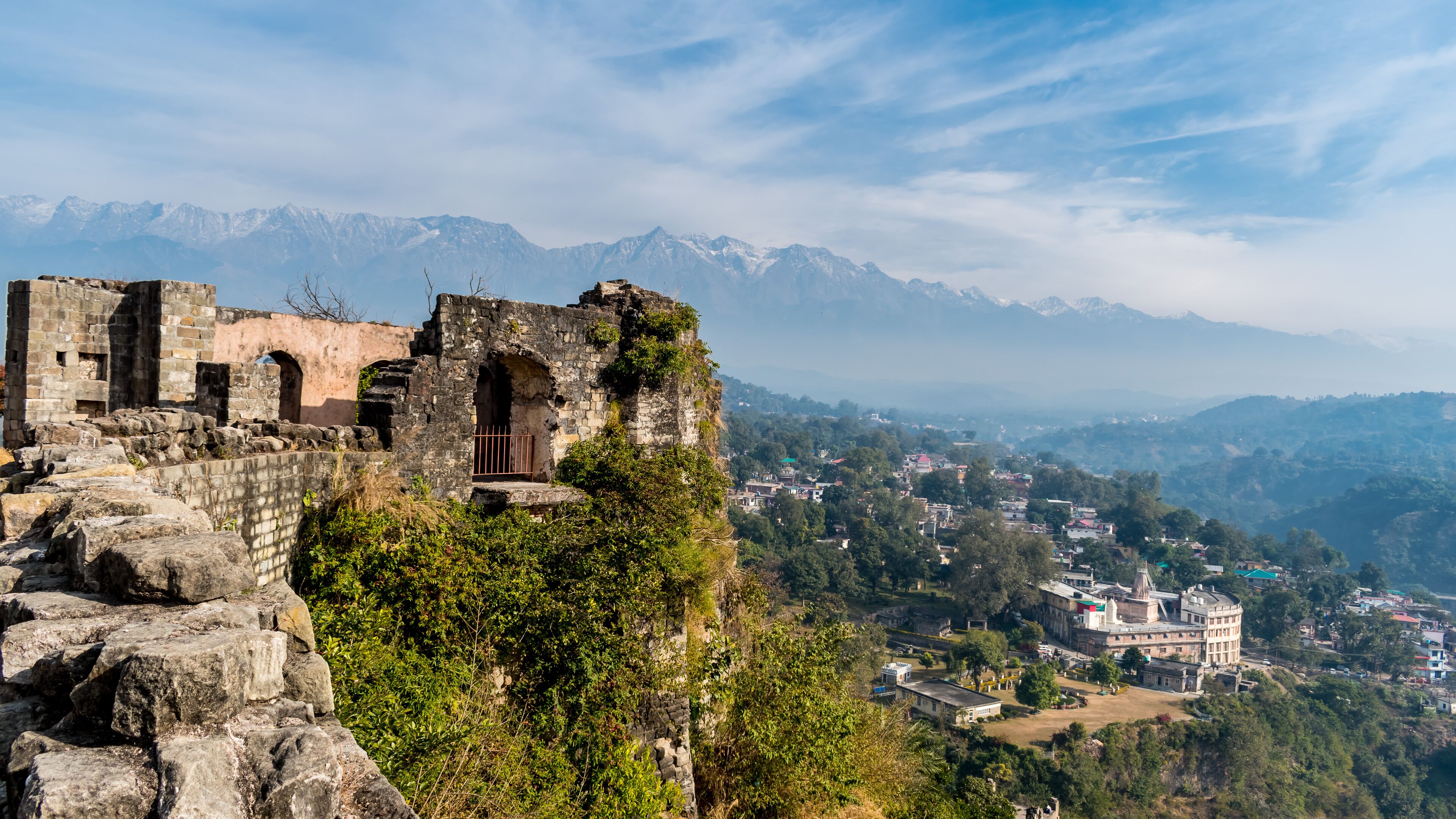 Ancient ruins on a cliff overlooking a town with mountains in the background.