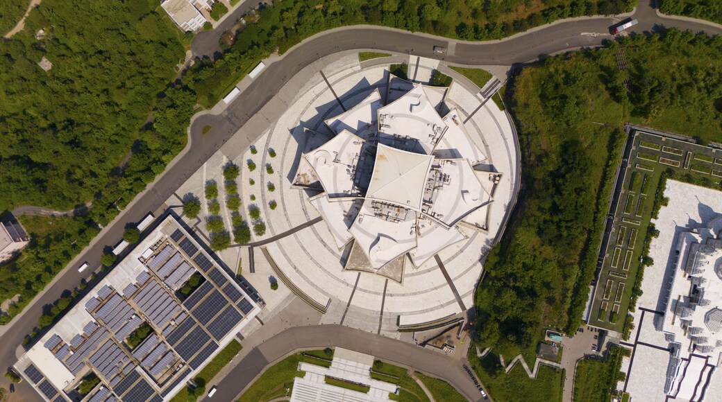 Aerial view of the white lotus-shaped temple surrounded by circular paved walkways, lush green trees, and a solar panel installation in Chikhli, Gujarat, India.