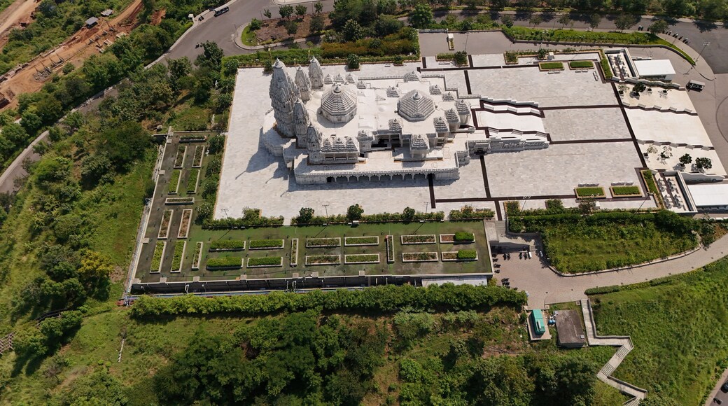 Aerial view of the white stone BAPS Shri Swaminarayan Mandir temple complex with intricate architecture, surrounded by landscaped gardens and paved courtyards in Chikhli, Gujarat, India.