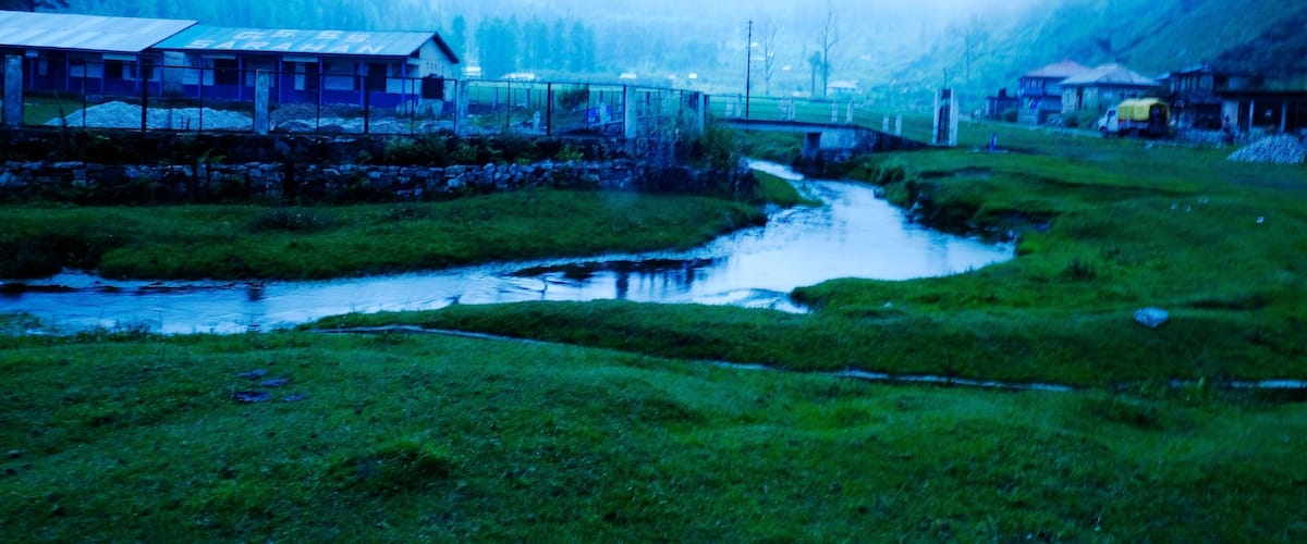 A misty valley with a small bridge, a river, and houses surrounded by forest.