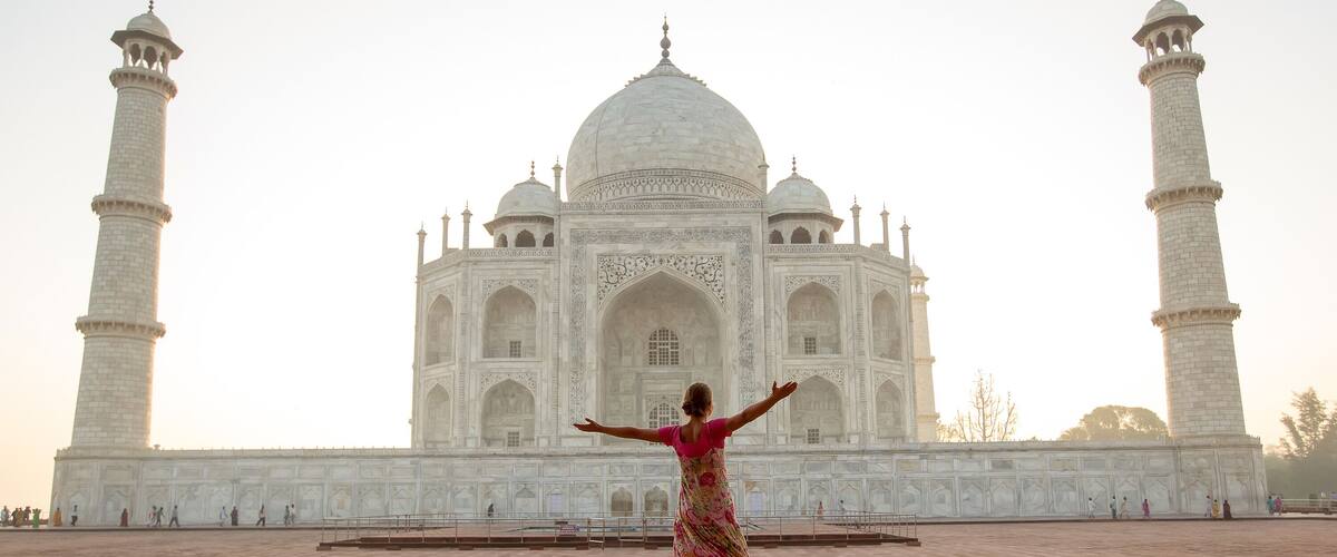 A person in a floral dress standing in front of the Taj Mahal with arms outstretched.